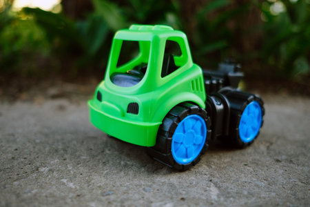 A vibrant green toy truck with blue wheels rests on a gravel surface Sunlight shines gently illuminating the toy against the backdrop of lush greenery creating a cheerful atmosphere.の写真素材
