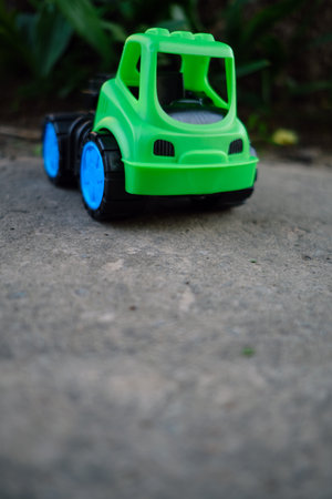 A vibrant green toy truck with blue wheels rests on a gravel surface Sunlight shines gently...