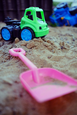 A bright green toy truck rests on a sandy surface highlighting outdoor playtime Nearby a blue toy vehicle lies overturned in the background adding to the construction theme of the scene.の写真素材