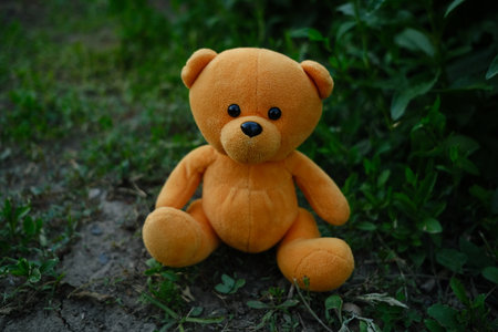 A plush teddy bear with vibrant orange fur is placed on the ground amidst lush green grass and...