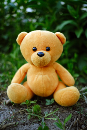 A plush teddy bear with vibrant orange fur is placed on the ground amidst lush green grass and...