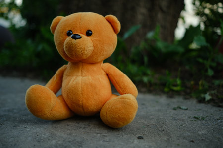 A soft orange teddy bear is positioned on the ground with a backdrop of lush greenery The warm late afternoon light casts gentle shadows creating a peaceful atmosphere around the toy.の写真素材