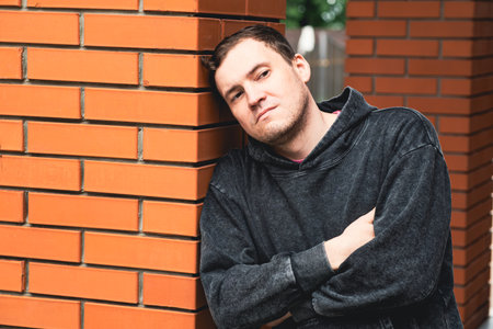 Man Leaning Against Brick Pillar in Urban Setting During Daytime Deep in Thought.の写真素材