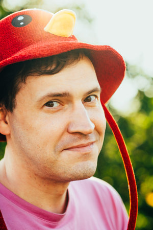 Man Wearing a Red and Yellow Playful Hat Enjoys a Sunny Outdoor Moment Surrounded by Trees in a...