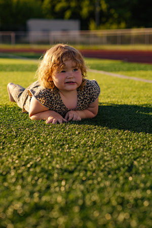A young child with curly hair smiles while crawling on a green grassy surface The sun creates a warm glow illuminating the playful scene during late afternoonの写真素材