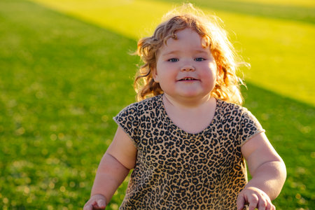 A cheerful child with curly hair smiles while playing in a vibrant green field under bright sunlight...