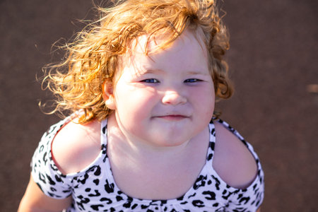 Child with curly red hair is smiling cheerfully while playing outside on a sunny day The vibrant atmosphere reflects joy and innocence in carefree surroundings.の写真素材