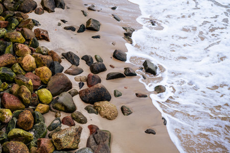 Colorful rocks of various sizes and shapes are scattered along a sandy beach Gentle waves roll in softly creating a peaceful seaside atmosphere.の写真素材
