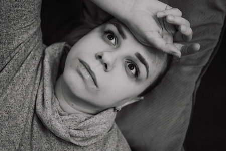 A woman reclines on a couch her expression pensive as she rests her hand on her forehead The cozy atmosphere suggests a moment of reflection or contemplation at homeの写真素材