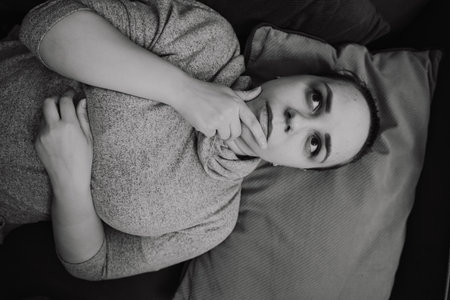 A woman rests on a couch lost in thought with her chin resting on her hand The soft lighting creates...
