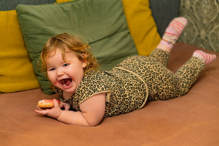 Child Enjoys Colorful Dessert While Lounging on a Couch in a Cozy Living Room During the Afternoonの写真素材