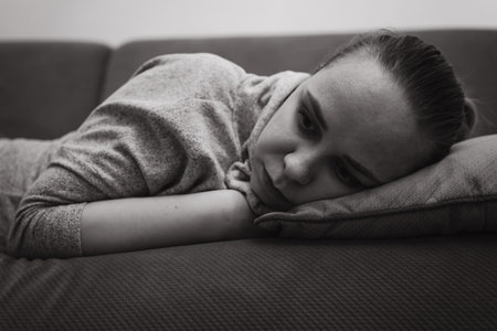 A young woman relaxes on a couch resting her head on a pillow while lost in thought The room has a calm atmosphere perfect for introspection during the afternoonの写真素材