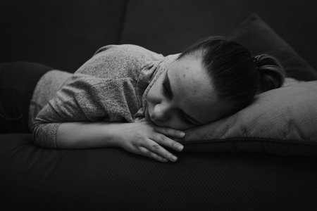 A young woman relaxes on a couch resting her head on a pillow while lost in thought The room has a...