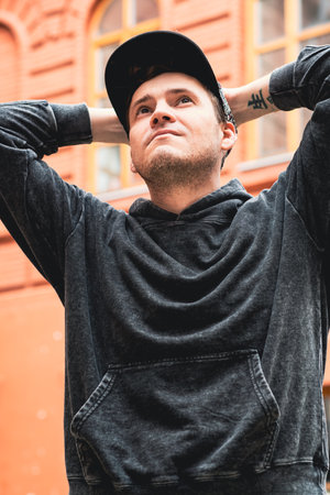 A man stands with hands on his head wearing a black hoodie and cap He looks contemplative in front...