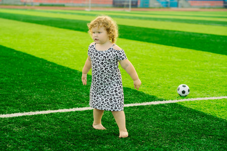 A young girl with curly hair stands confidently on a vibrant green soccer fieldの写真素材
