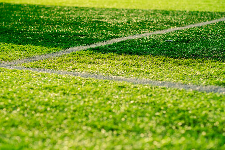 Bright green artificial turf covers the football field with white lines marking boundaries Sunlight...