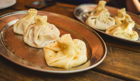 Delicious khinkali traditional Georgian dumplings filled with meat are beautifully arranged on a metal platter garnished with spices in a warm dining settingの写真素材