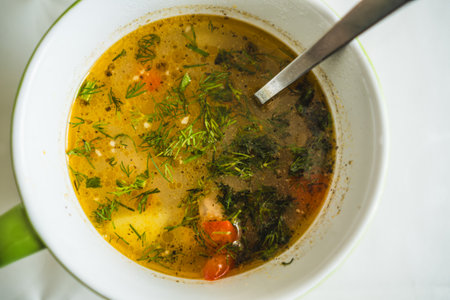 A steaming bowl of hearty soup filled with colorful vegetables and garnished with fresh herbs sits on a kitchen table Perfect for a comforting meal during cold daysの写真素材