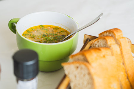 A steaming bowl of hearty soup filled with colorful vegetables and garnished with fresh herbs sits on a kitchen table Perfect for a comforting meal during cold daysの写真素材