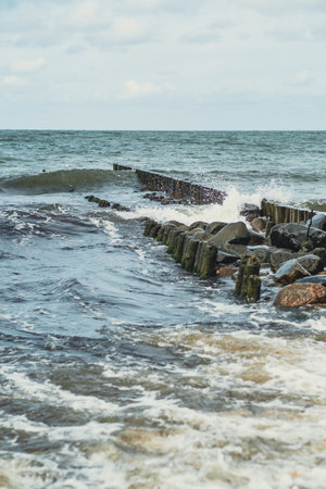 Waves crash powerfully against a coastal breakwater as the ocean churns under cloudy skies. The structure protects the shoreline from erosion and enhances the landscapeの写真素材