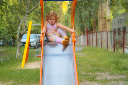 Child preparing to slide down a playground slide in a sunny outdoor play area.の写真素材