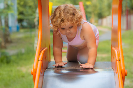 Child preparing to slide down a playground slide in a sunny outdoor play area.の写真素材