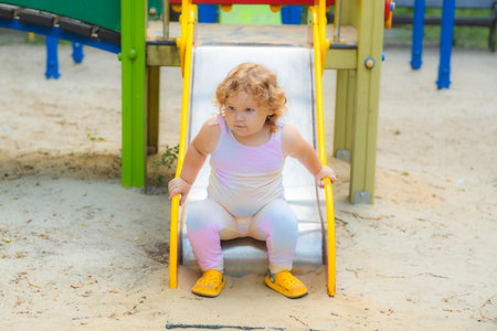 A young child with curly hair slides down a colorful slide at a park. The sun shines, creating a joyful atmosphere for outdoor playの写真素材