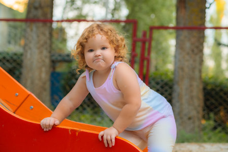 A young child with curly hair slides down a colorful slide at a park. The sun shines, creating a joyful atmosphere for outdoor playの写真素材