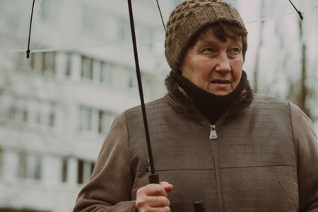 Thoughtful woman holding a transparent umbrella on a rainy day in an urban environment while...