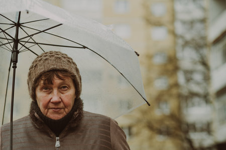 Thoughtful woman holding a transparent umbrella on a rainy day in an urban environment while contemplating life.の写真素材