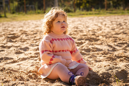 Child playing in sandy area wearing warm sweater on a bright sunny day outdoors.の写真素材