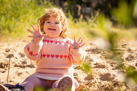 Child playing in sandy area wearing warm sweater on a bright sunny day outdoors.の写真素材