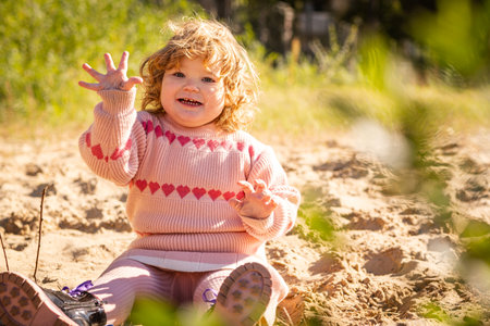 Child playing in sandy area wearing warm sweater on a bright sunny day outdoors.の写真素材