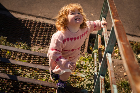 Young child exploring stairs at a park on a sunny afternoon in a cozy pink sweaterの写真素材