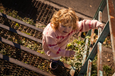 Young child exploring stairs at a park on a sunny afternoon in a cozy pink sweaterの写真素材