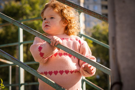 Young child exploring stairs at a park on a sunny afternoon in a cozy pink sweaterの写真素材