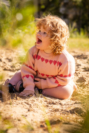 Child playing in sandy area wearing warm sweater on a bright sunny day outdoors.の写真素材
