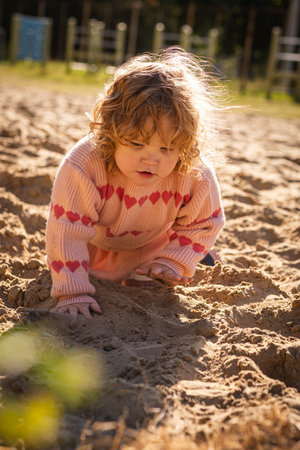 Child playing in sandy area wearing warm sweater on a bright sunny day outdoors.の写真素材
