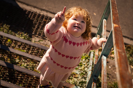 A young child with curly hair joyfully points upward while ascending a set of stairs. The scene...