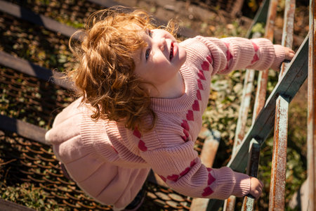 Young child exploring stairs at a park on a sunny afternoon in a cozy pink sweaterの写真素材
