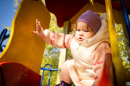 A young child enjoys playing on a playground in a lovely park. Dressed warmly, the child smiles while exploring the climbing structure under a clear blue sky.の写真素材