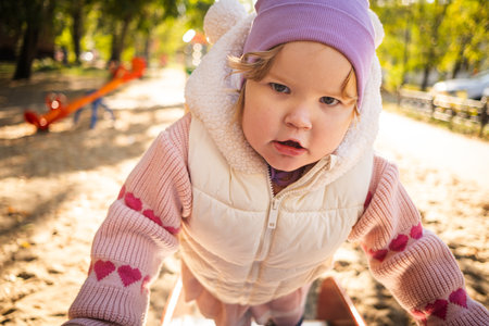 A young child enjoys playing on a playground in a lovely park. Dressed warmly, the child smiles while exploring the climbing structure under a clear blue sky.の写真素材
