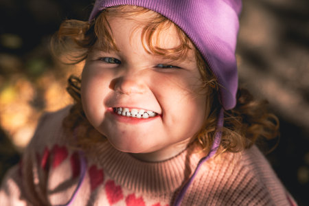 Happy child in a purple hat smiles brightly during autumn playtime in the parkの写真素材