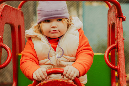 Child enjoys driving a colorful toy car at a playground on a crisp day in autumn with vibrant colors surrounding the sceneの写真素材