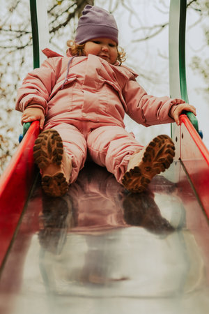 Child enjoys sliding down vibrant slide in a colorful park during autumn.の写真素材