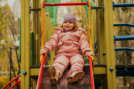 Child enjoys sliding down vibrant slide in a colorful park during autumn.