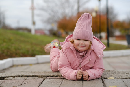 Child Enjoying a Playful Moment on a Pathway in a Park During a Cloudy Day in Autumnの写真素材