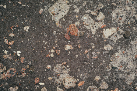 Old Asphalt Surface With Gravel and Stones Showing Natural Weathering and Texture in an Outdoor Settingの写真素材
