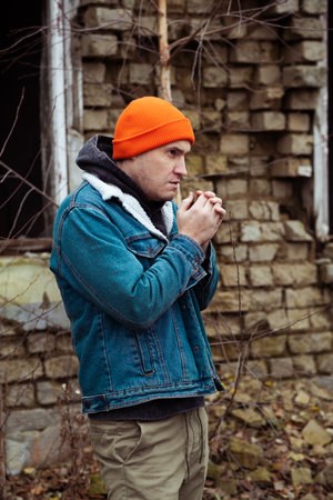 A man with an orange beanie and denim jacket is outside in a cold environment He is holding his...