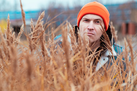 A man wearing an orange beanie looks directly at the camera surrounded by tall golden grass in a natural environment The weather appears overcast giving a moody feelの写真素材